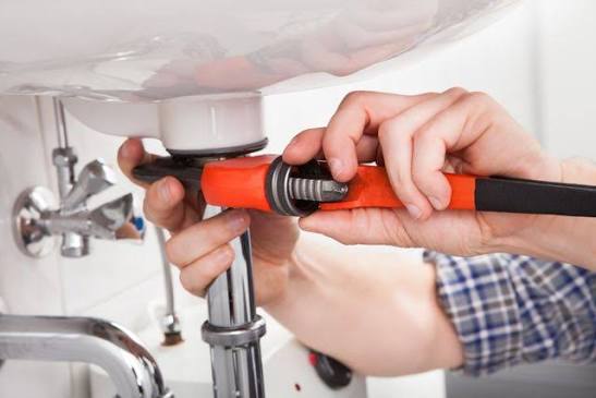 Plumber repairing pipes under a bathroom sink